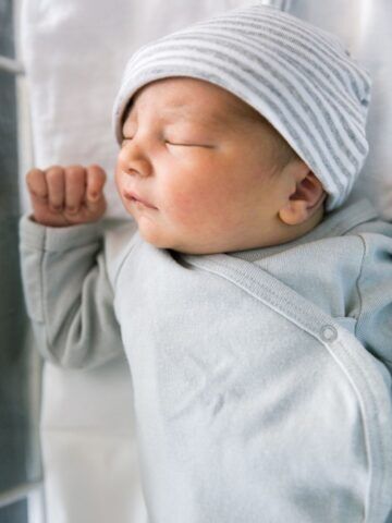 newborn in hat sleeping on back