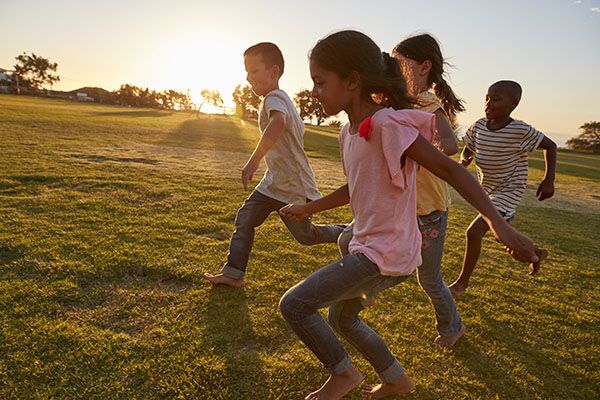 Four children running barefoot across a lawn at sunset