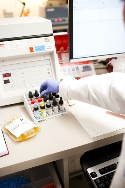 Person in white coat with gloved hand conducting research.