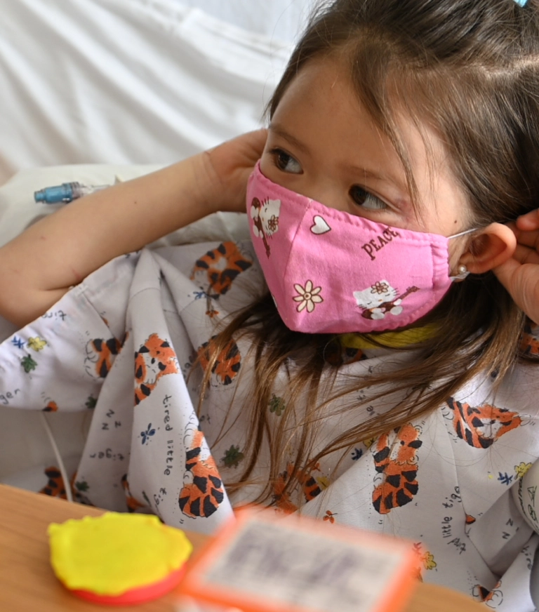 girl in hospital bed wearing a pink mask