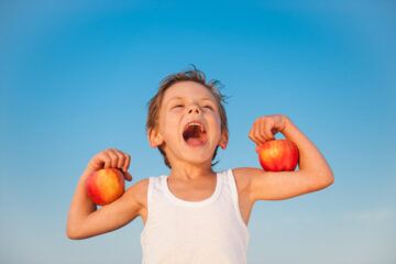 child holding up muscles with apples on his arms