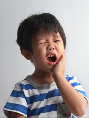 young boy holding his face in pain because he has a tooth ache