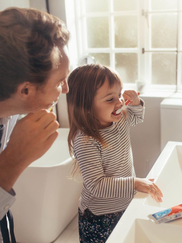 Father and daughter brushing teeth in bathroom