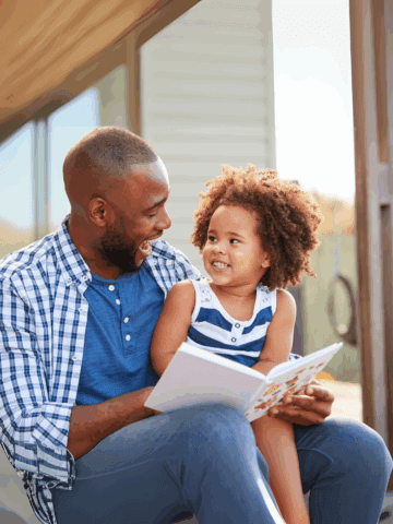 Father raising a summer reader - reading book outside with daughter