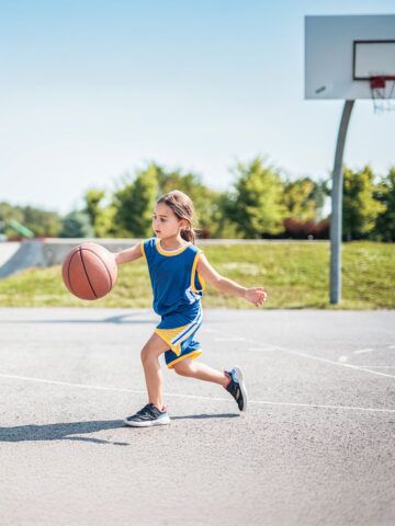 A child girl with basketball on court on summer season