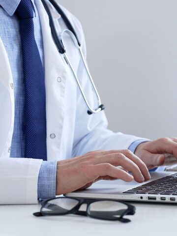 Medical professional typing on laptop, updating electronic patient records with focused concentration, representing digital transformation in healthcare workplace