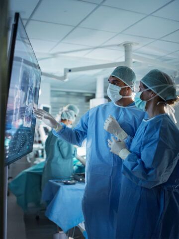 Caucasian Male and Female Surgeons Analyze Scans on a Digital Monitor, Planning Surgical Strategy in a High-tech Operating Room. Colleagues Working Together, Preparing for Surgery