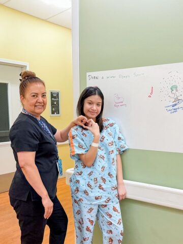 A mental health assistant and patient smile beside the patient’s whiteboard drawing.